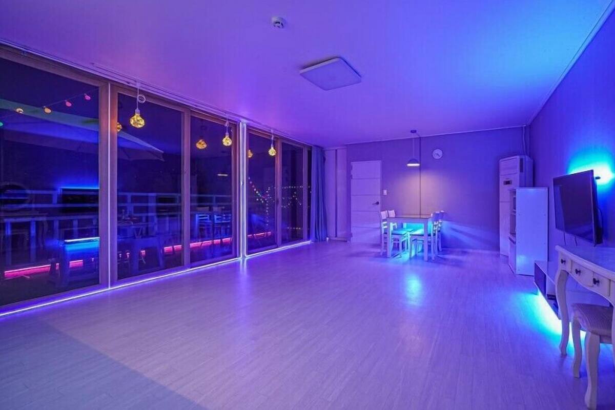 A modern room with a large sliding glass door leading to a balcony, a dining area with a table and chairs, and a television on a stand.
