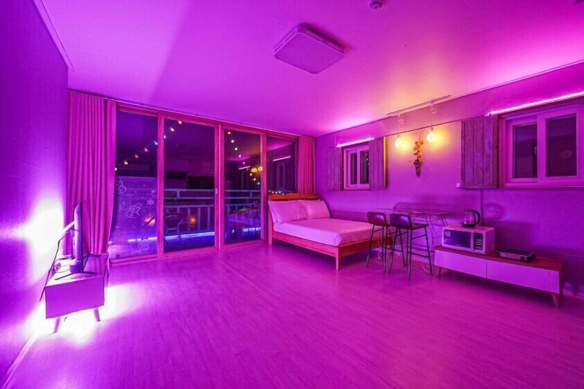 A room with a bed, a desk, and a dining area. There is a large window and a door leading to an outdoor balcony.