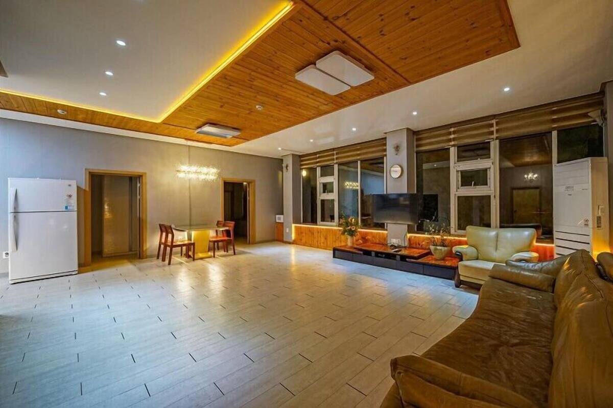 A spacious living room with a wooden ceiling, a large sofa, a dining area with chairs, and a television.