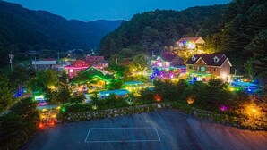 A residential area with houses decorated with colorful lights, a basketball court, and a mountainous backdrop. - Sunny Hill Pension (Gapyeong)