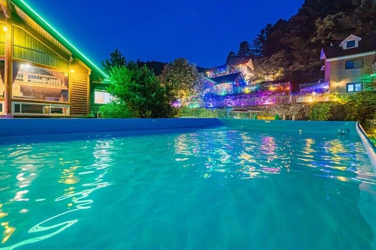 A swimming pool with a wooden deck and a building with colorful lighting.