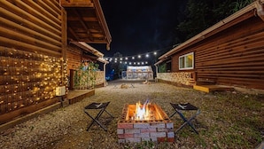 A wooden cabin with a fire pit in the center, surrounded by seating and string lights. - Sunny Hill Pension (Gapyeong)