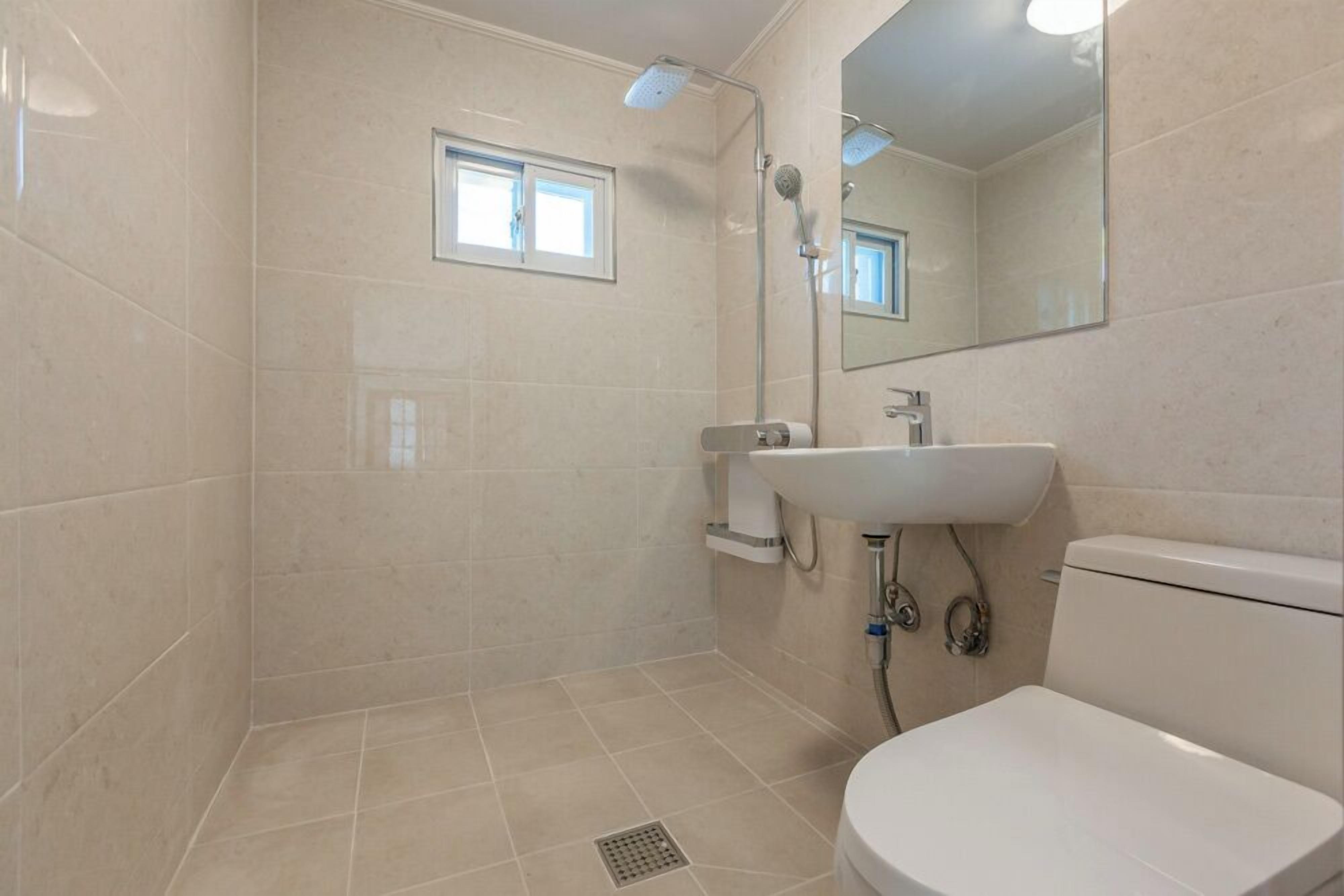 Un baño con ducha, inodoro, lavamanos y ventana.