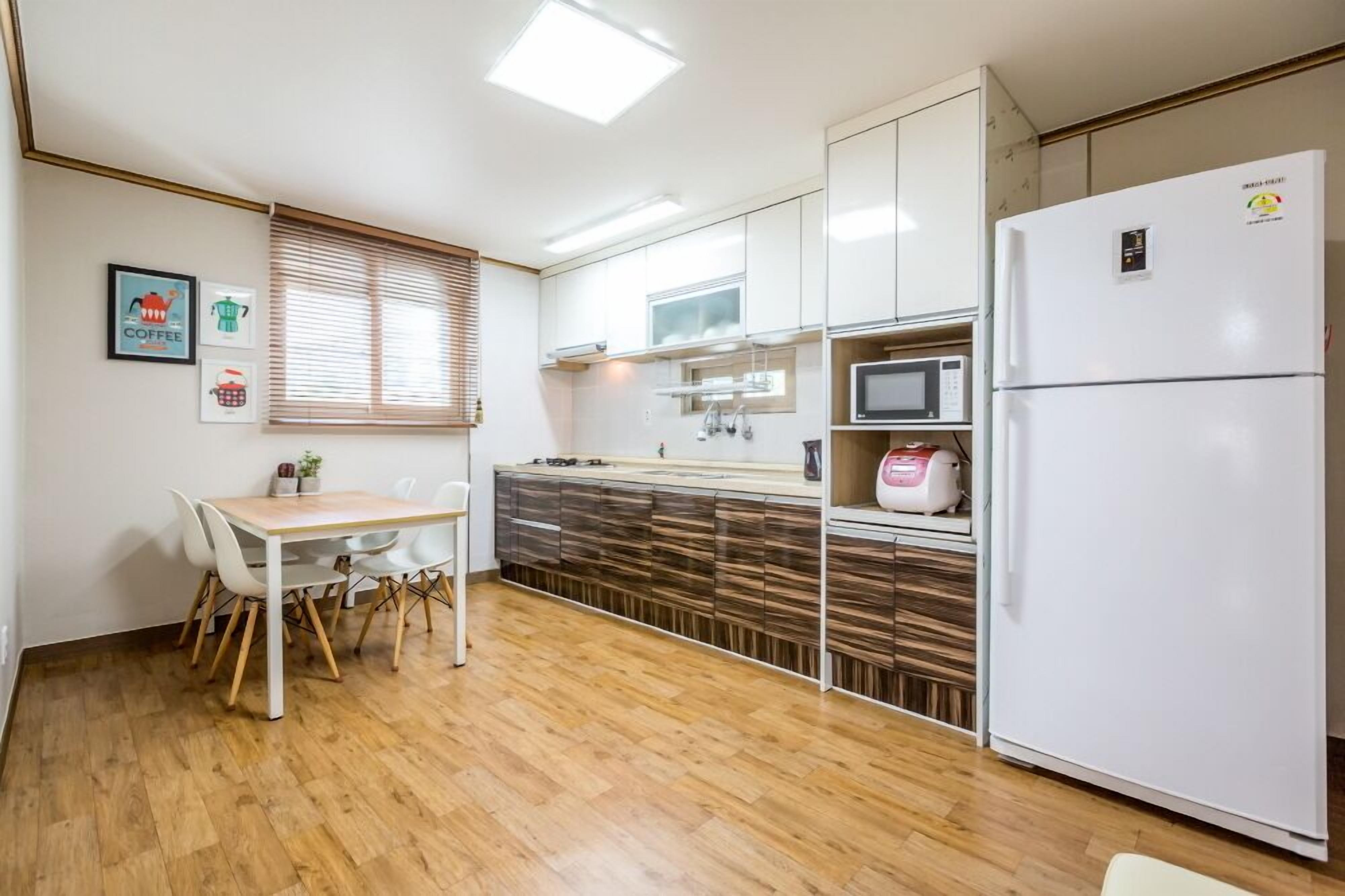Une cuisine moderne avec des meubles blancs, un four à micro-ondes, un réfrigérateur et un coin repas comprenant une table et des chaises.