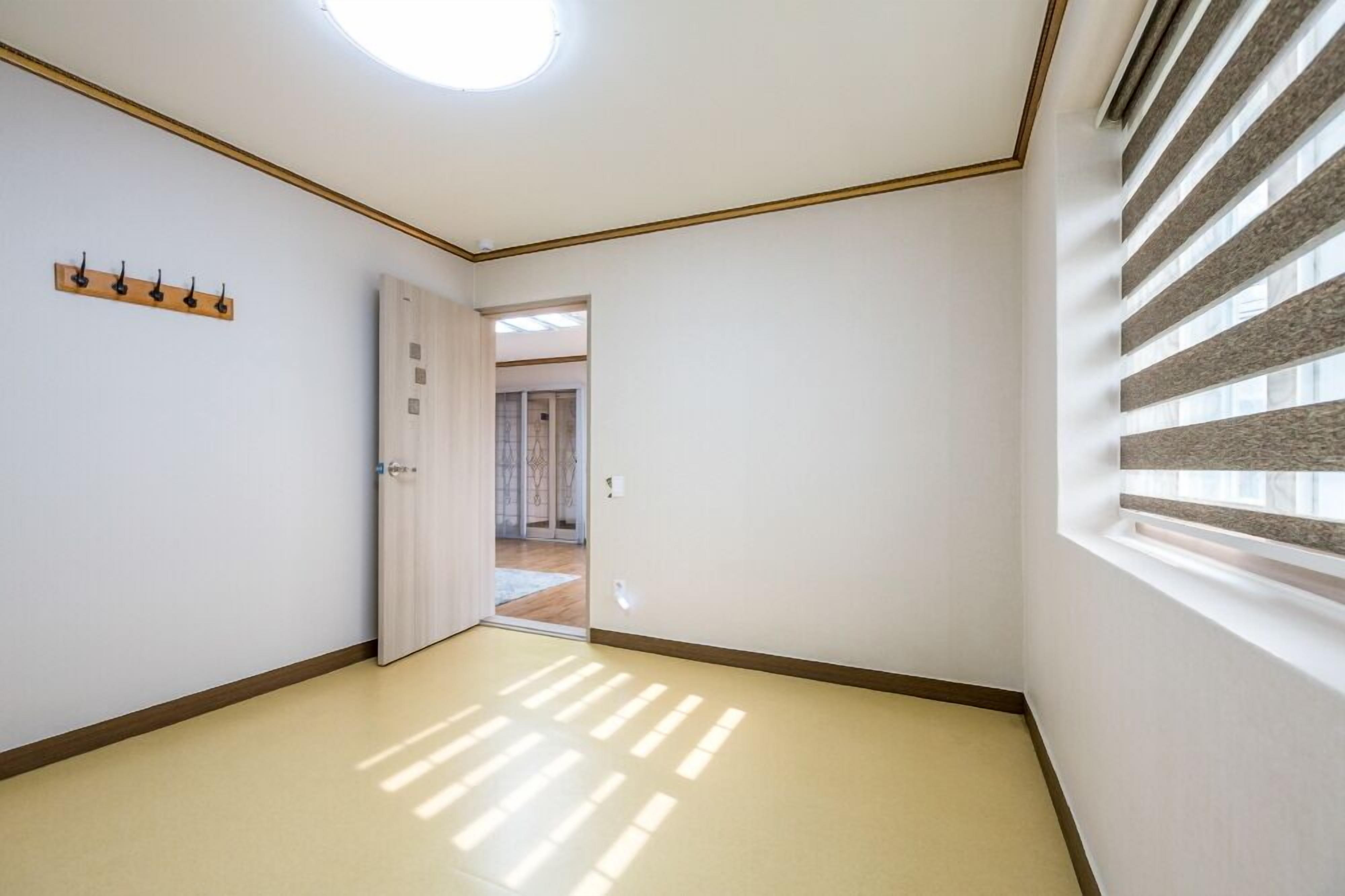 A hallway with a wooden floor, a ceiling light, a coat rack, and a door leading to another room.