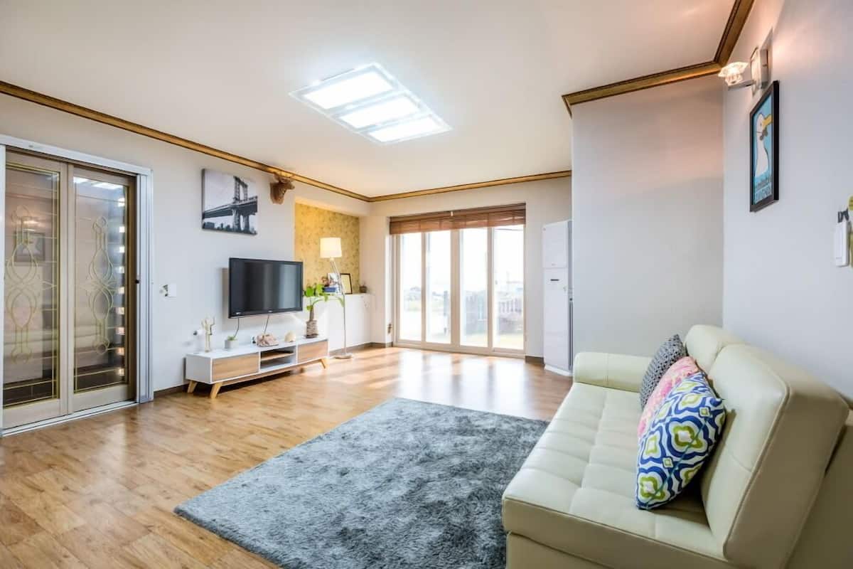 A modern living room with a flat-screen TV, a sofa, a coffee table, and a large window.