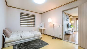 A bedroom with a bed, bedside table, lamp, and a view into another room.