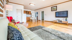 Una sala de estar moderna con un sofá, un televisor y una cocina al fondo.