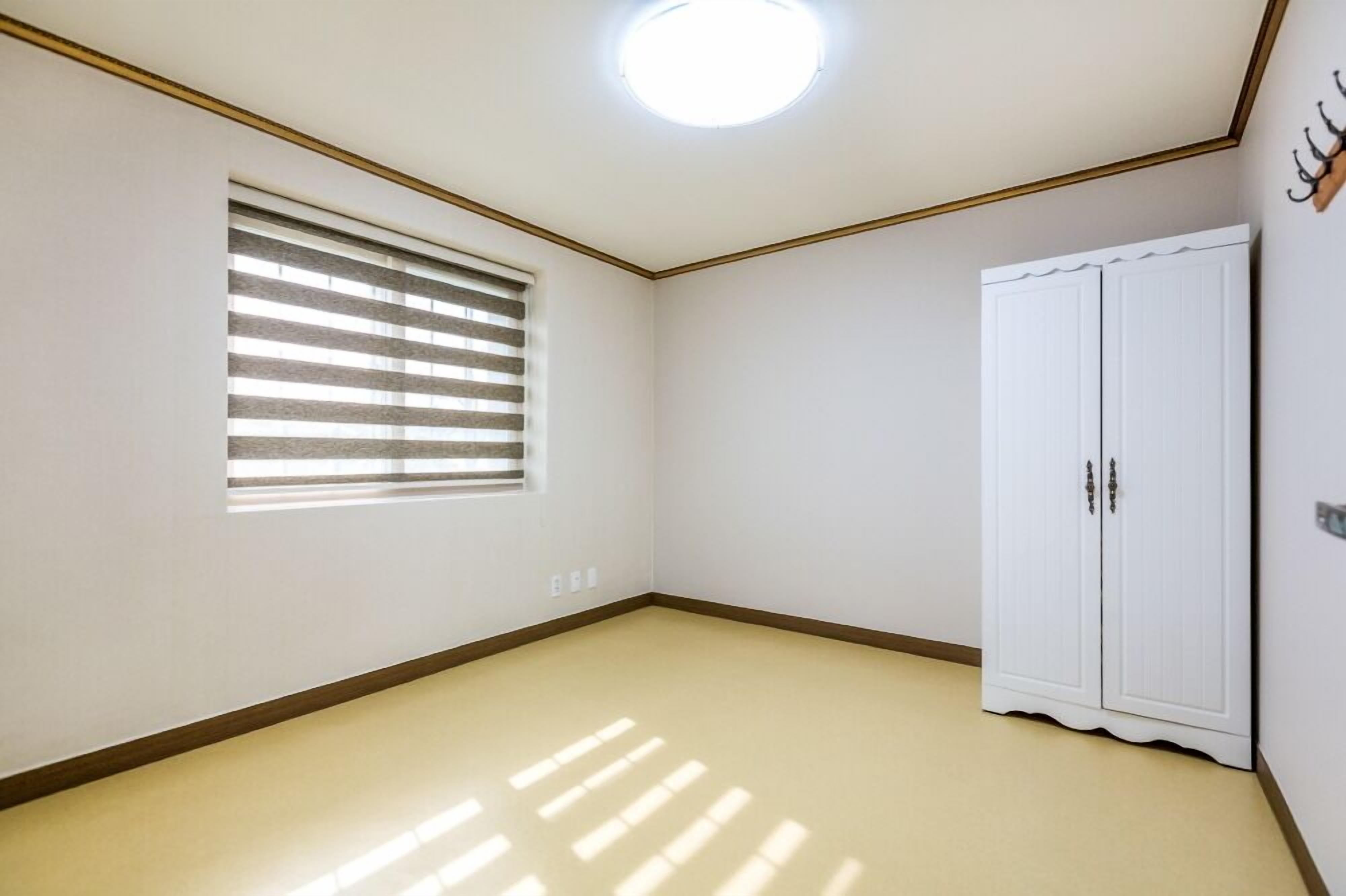 A room with a ceiling light, a window with blinds, and a white wardrobe.
