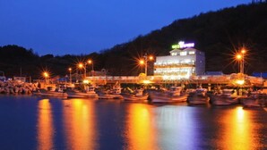 Un hôtel situé au bord de l’eau, avec plusieurs bateaux amarrés devant, un bâtiment bien éclairé avec une enseigne, et une étendue d’eau calme qui reflète les lumières.
