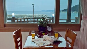 Une table avec vue sur la mer, une horloge, une plante et deux verres de jus d’orange.