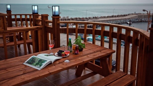 Une terrasse en bois avec une table dressée pour deux personnes, agrémentée d’un livre, de verres et d’une bouteille de vin.