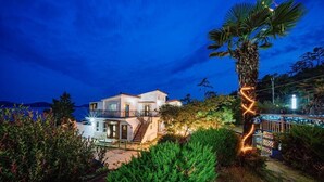 A two-story house with a balcony, surrounded by lush greenery and a palm tree. - Santamonica Pension (Geoje)