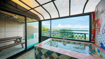 A room with a large window, a bench, and a tiled hot tub.