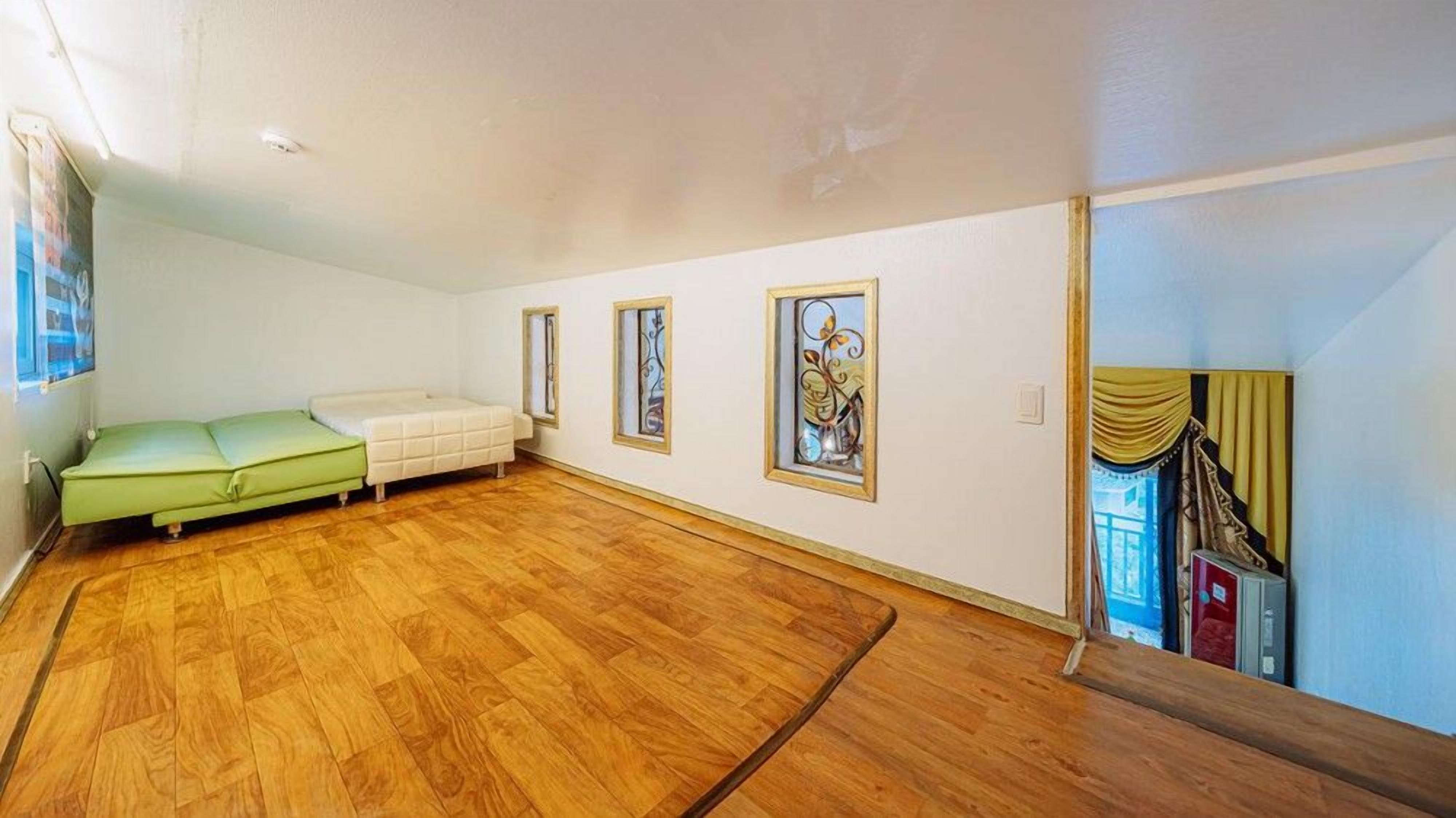 Una habitación con un sofá verde, una cama blanca, suelo de madera y tres cuadros en la pared.