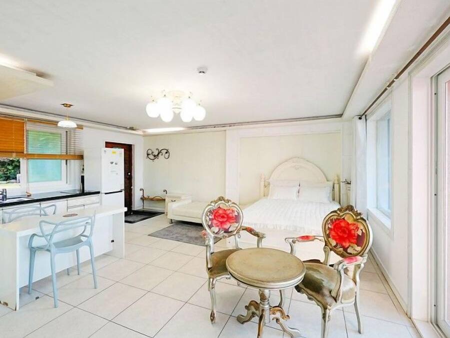 Habitación de hotel con cama, zona de comedor con mesa y sillas, kitchenette y un ventanal grande.