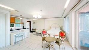 Een hotelkamer met een bed, een zithoek met een tafel en stoelen, een kitchenette en een groot raam.