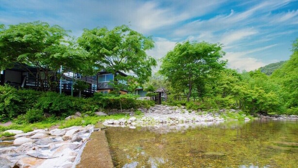Un cadre paisible au bord de la rivière, offrant une vue dégagée sur un bâtiment moderne à plusieurs étages et sur une structure traditionnelle située à proximité.