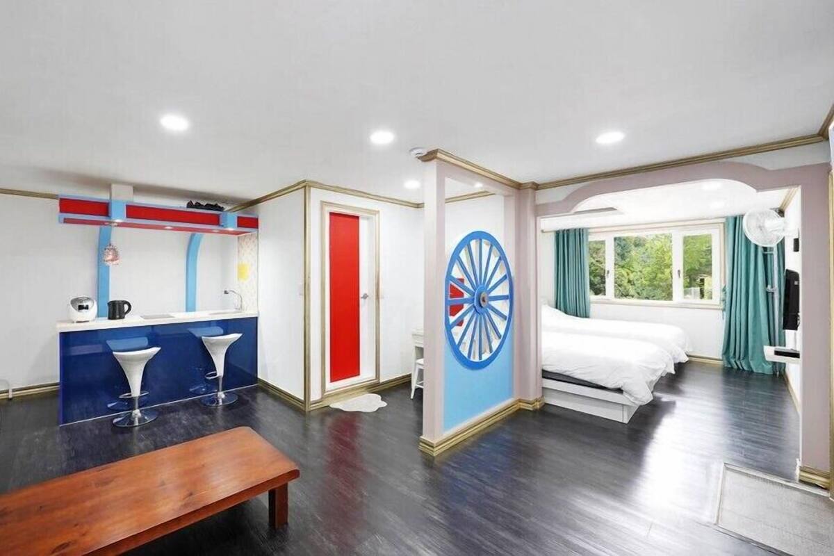 A room with a bed, a desk, a chair, a small table, a dartboard, and a window with curtains.
