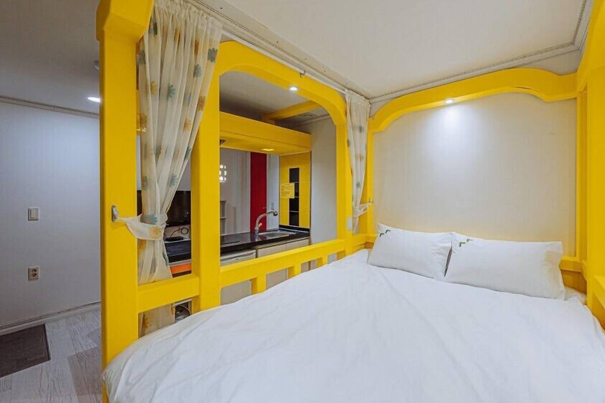 A room with a bed, a mirror, and a window with yellow trim.