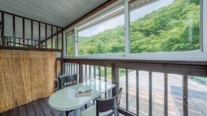 Un espace extérieur abrité, doté d’une table et de chaises en verre, qui offre une vue sur une forêt verdoyante et luxuriante.
