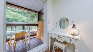 Une pièce dotée d’une terrasse en bois, d’une coiffeuse blanche avec un miroir et une lampe, et offrant une vue sur la verdure environnante.