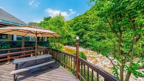 Une terrasse en bois avec un banc et un parasol, offrant une vue sur une rivière et une végétation luxuriante.