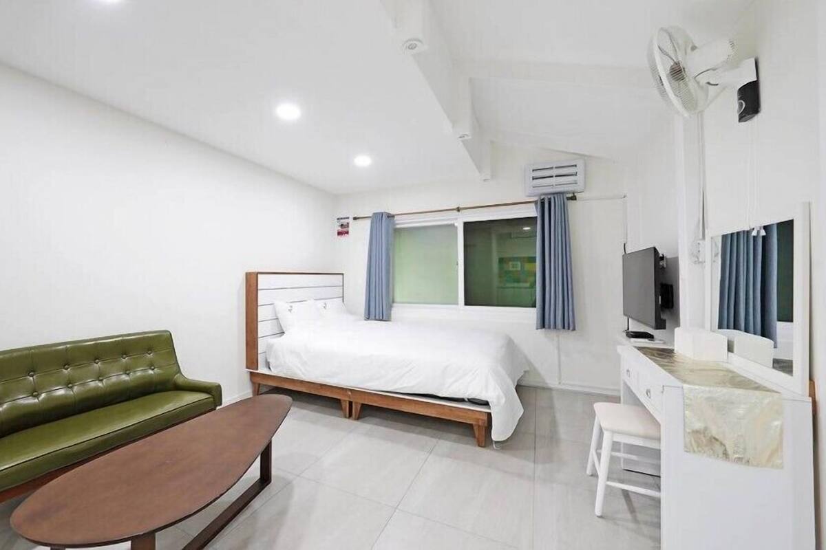 A hotel room with a bed, a green sofa, a small table, a TV, and a window with curtains.