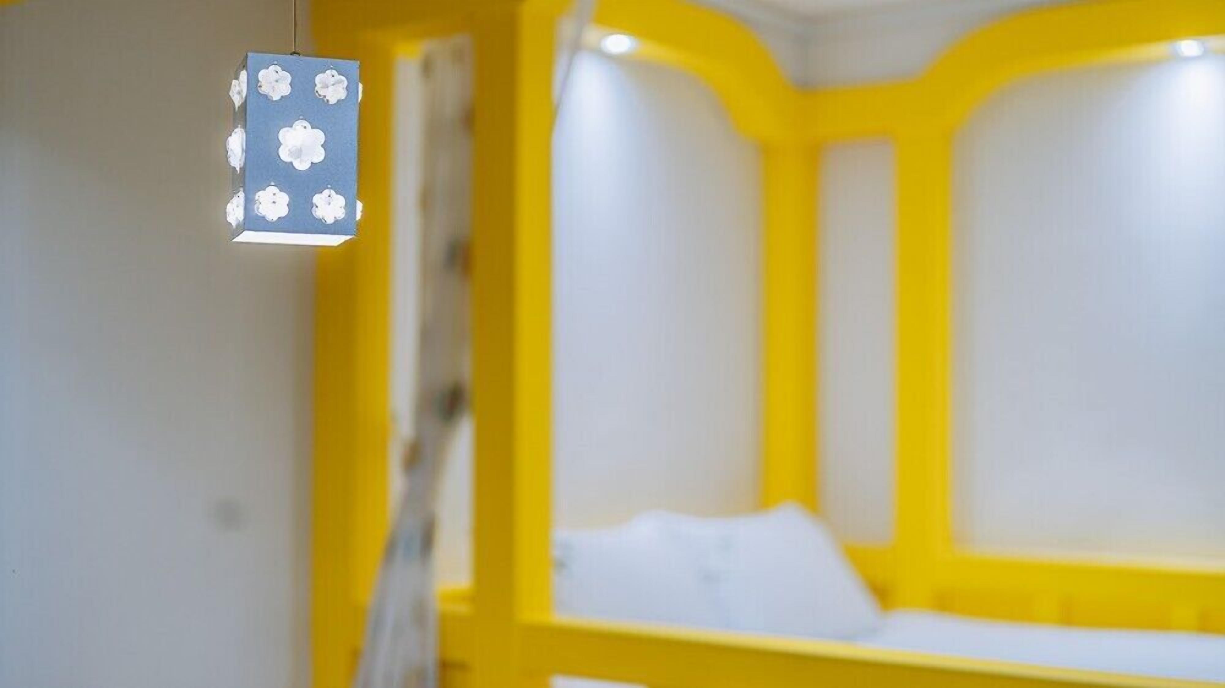 A room with a yellow and white color scheme, featuring a bed with white bedding and a hanging light fixture with a floral design.