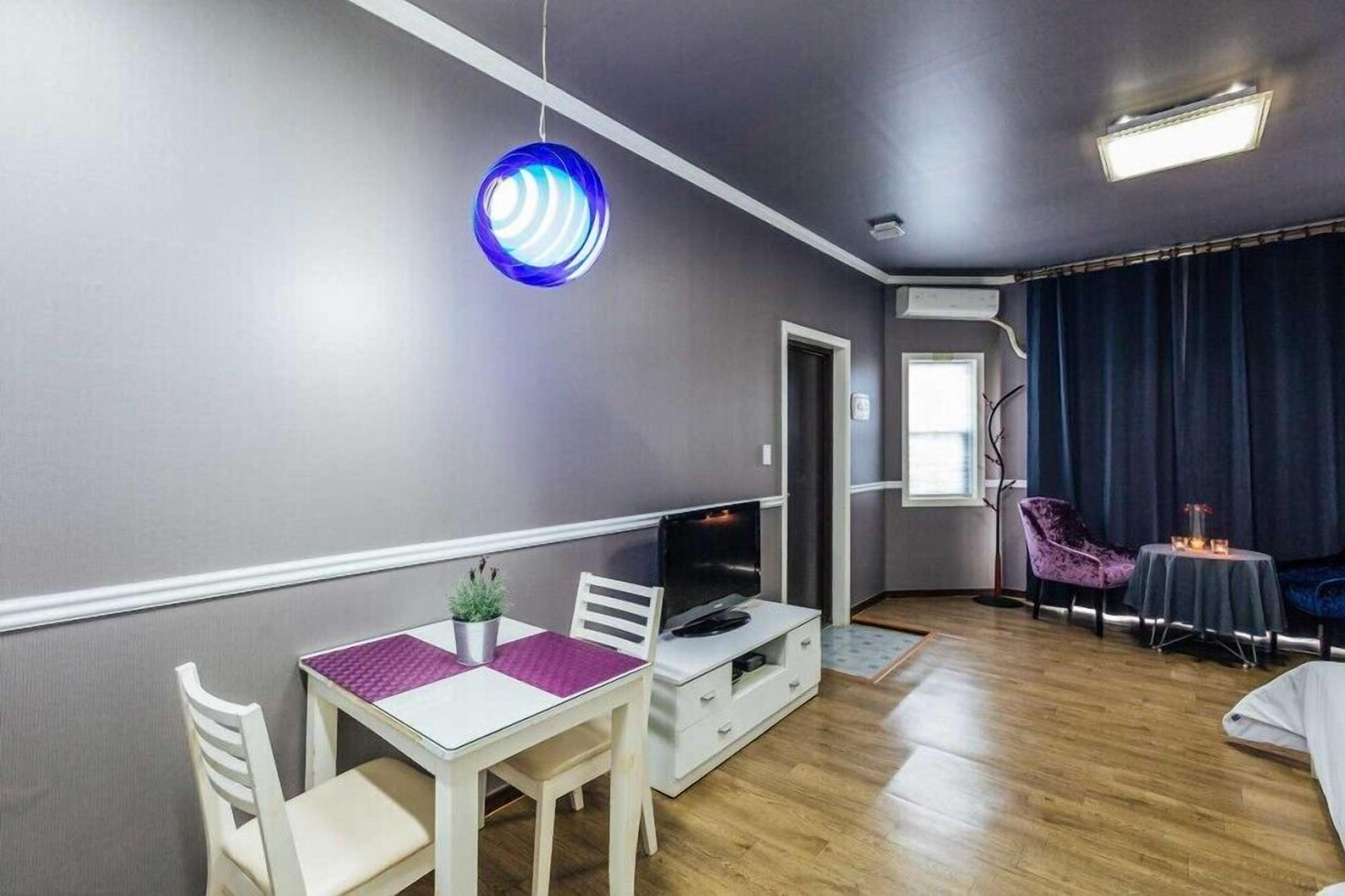 Een moderne woonkamer met een witte tv-meubel, een eettafel met stoelen, een paars vloerkleed en een blauwe ronde lamp.