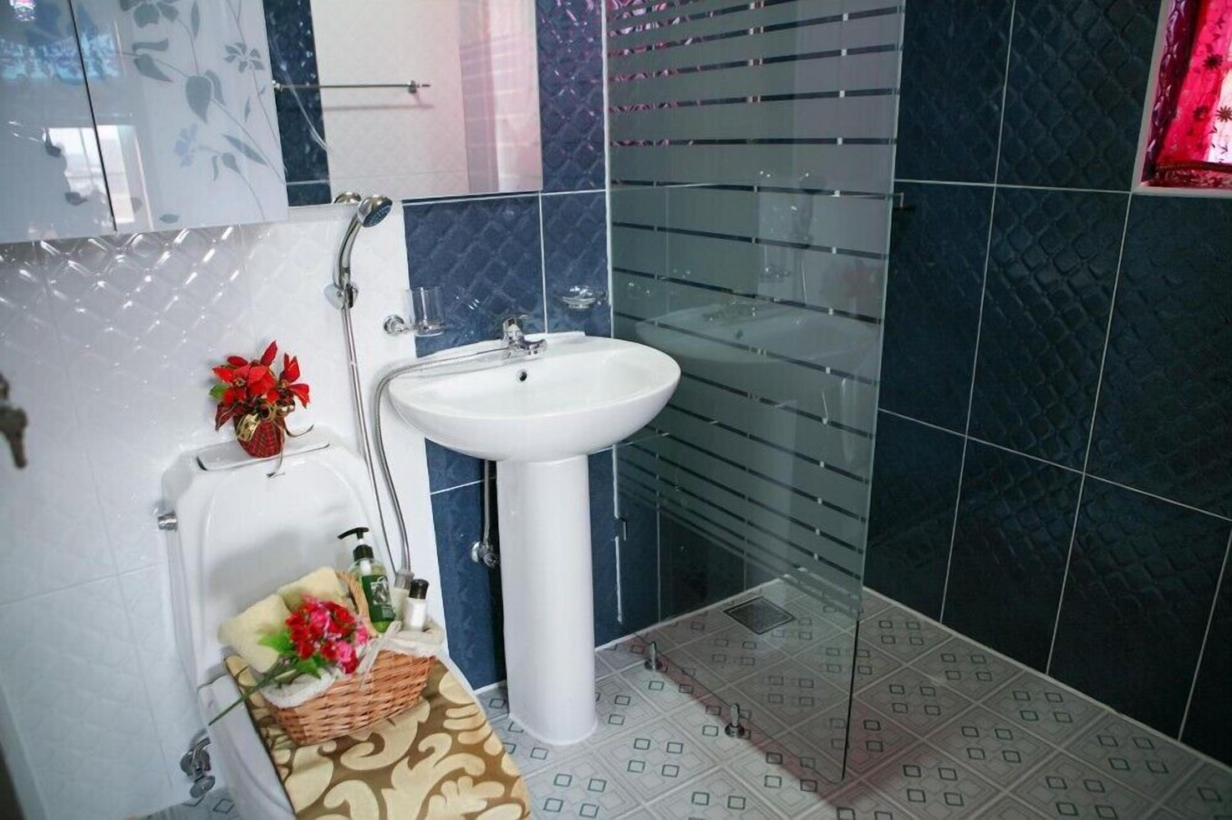 Um banheiro com pia branca, chuveiro e um cesto decorativo com flores.
