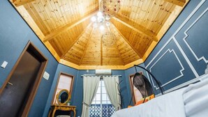 A room with a sloped wooden ceiling, a bed, a window with curtains, and a mirror on a dresser. - Indigo Pension (Hwaseong)
