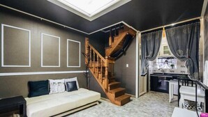 A room with a sofa, a wooden staircase, and a kitchen area. - Indigo Pension (Hwaseong)