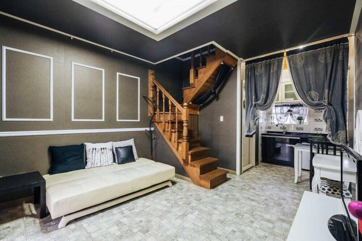 A room with a sofa, a wooden staircase, and a kitchen area.
