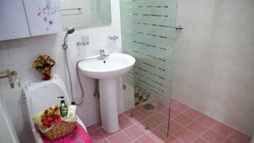 Un baño con un lavamanos blanco, cabina de ducha con mampara de vidrio y un inodoro con un cesto de flores.