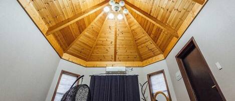 A room with a sloped wooden ceiling, a chandelier, a window, and a door.
