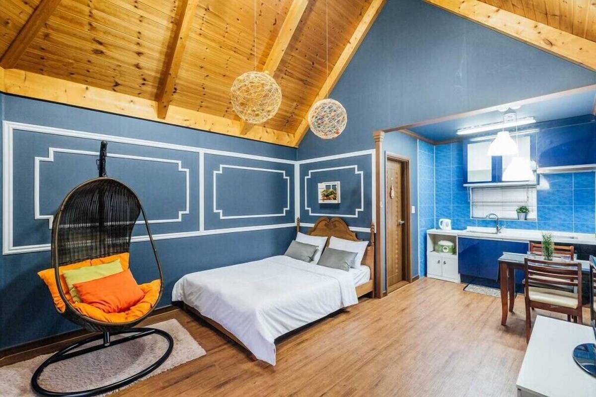 A bedroom with a bed, a hanging chair, and a kitchenette.