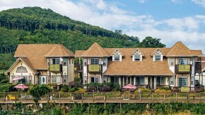 A row of traditional-style houses with pitched roofs, multiple windows, and balconies, set against a backdrop of lush green hills. - Indigo Pension (Hwaseong)