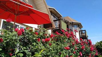 A house with a red umbrella, a balcony, and a garden with red flowers.
