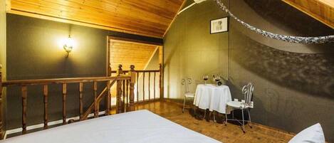 Ein gemütliches Zimmer mit Holzbalkendecke, einem Bett, einem kleinen Tisch mit Stuhl und einer Wandleuchte.