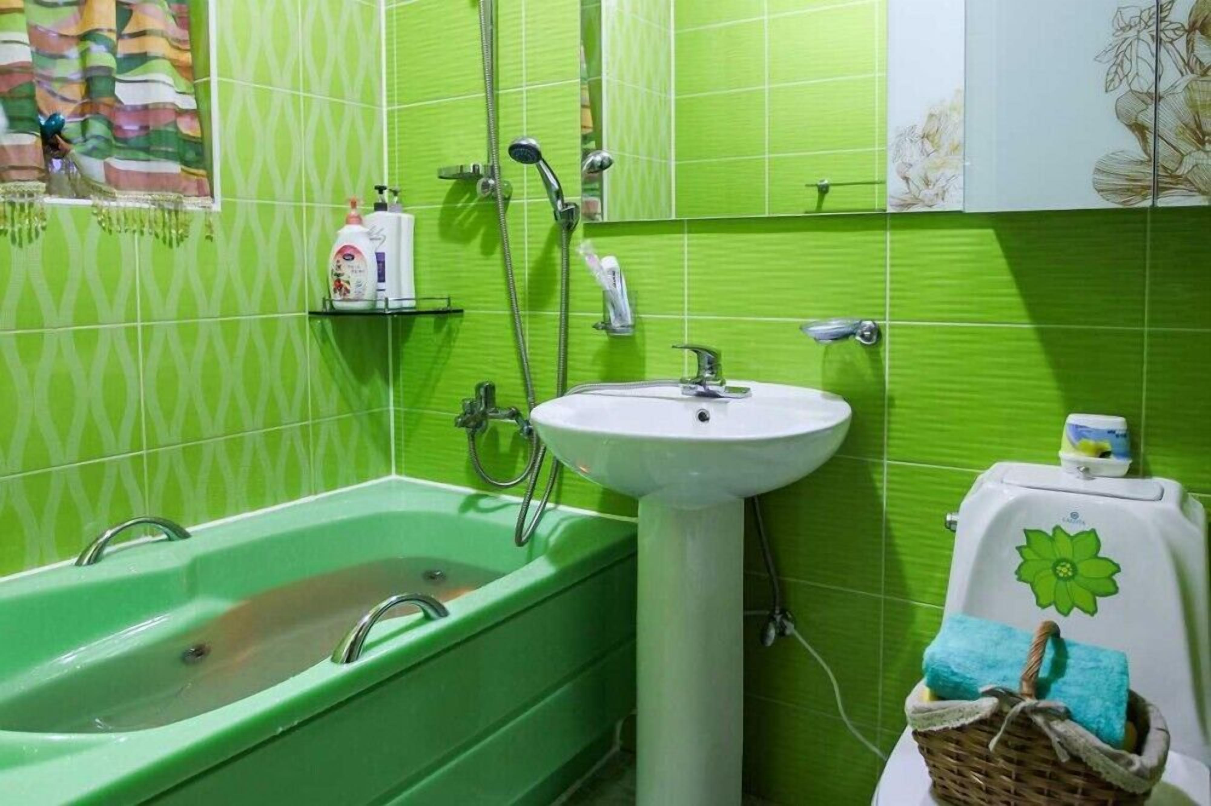 Een badkamer met een groen bad, een wit wastafel en een douche. Er is een plank met toiletartikelen en een mand met handdoeken.