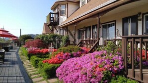 A two-story building with a porch and a garden with colorful flowers. - Indigo Pension (Hwaseong)