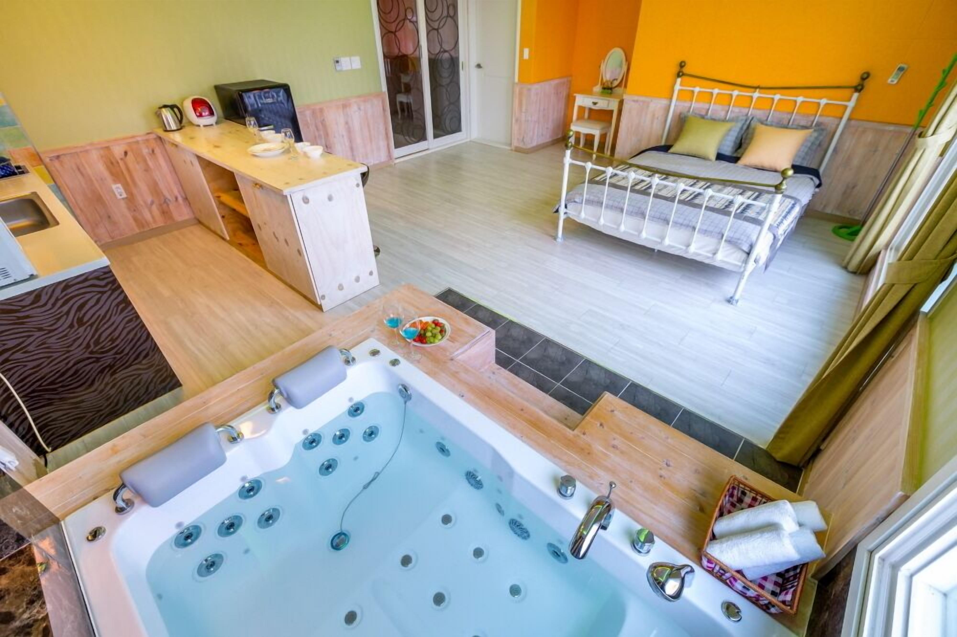 Una habitación con cama, escritorio, bañera y una pequeña mesa con un frutero.