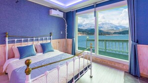 A bedroom with a bed, a window with a view of mountains and water, and a balcony railing. - Hosu Ilchul Pension (Jecheon)
