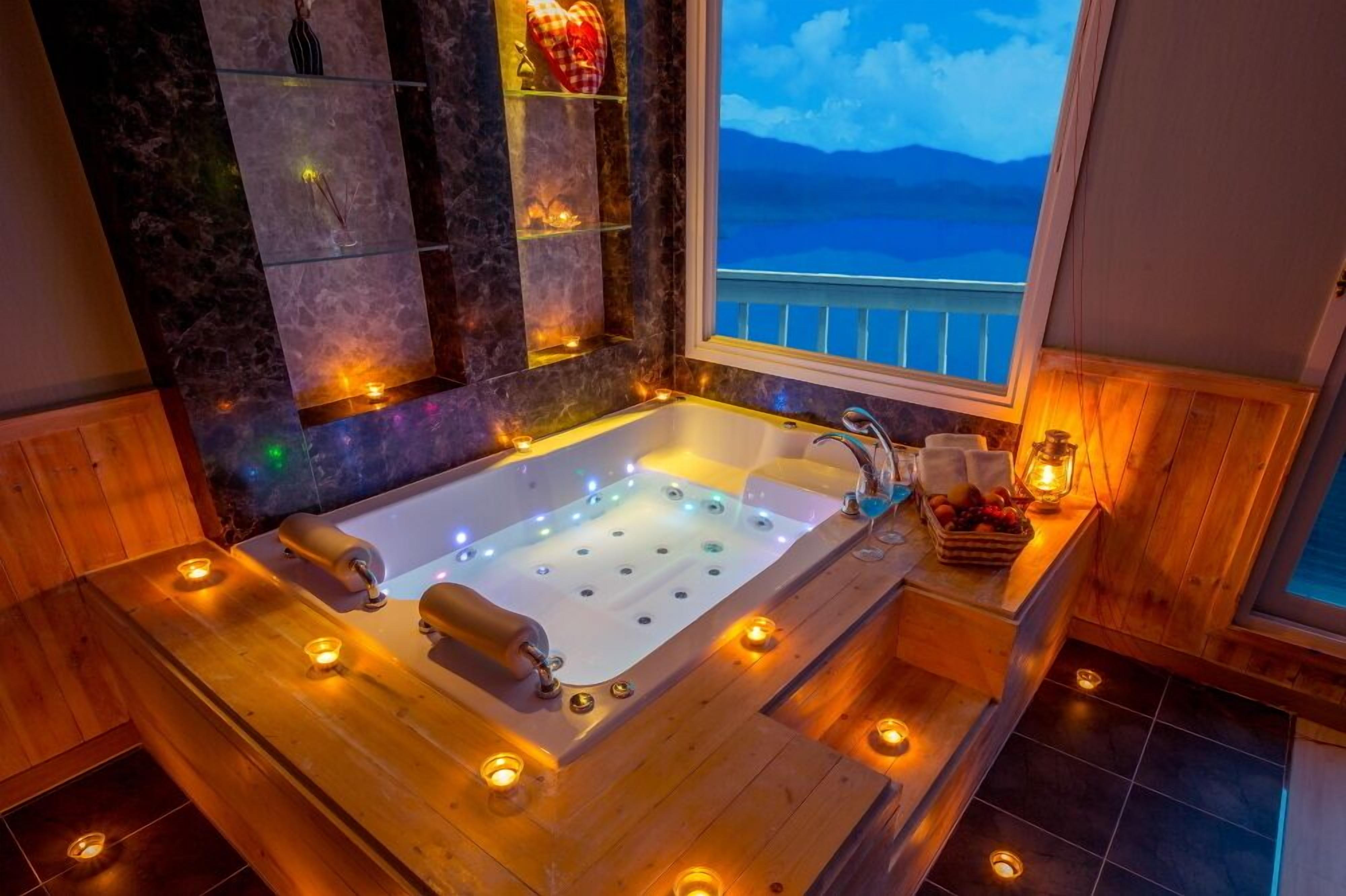Un cuarto de spa con una bañera grande, piso de madera y vista al mar por una ventana.