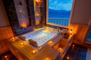 A spa room with a large bathtub, wooden flooring, and a view of the sea through a window. - Hosu Ilchul Pension (Jecheon)