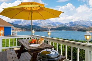 A wooden deck with a table, a grill, and an umbrella overlooking a lake with mountains in the background. - Hosu Ilchul Pension (Jecheon)