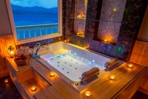 A large, rectangular hot tub with multiple jets, surrounded by wooden flooring and lit by candles. - Hosu Ilchul Pension (Jecheon)