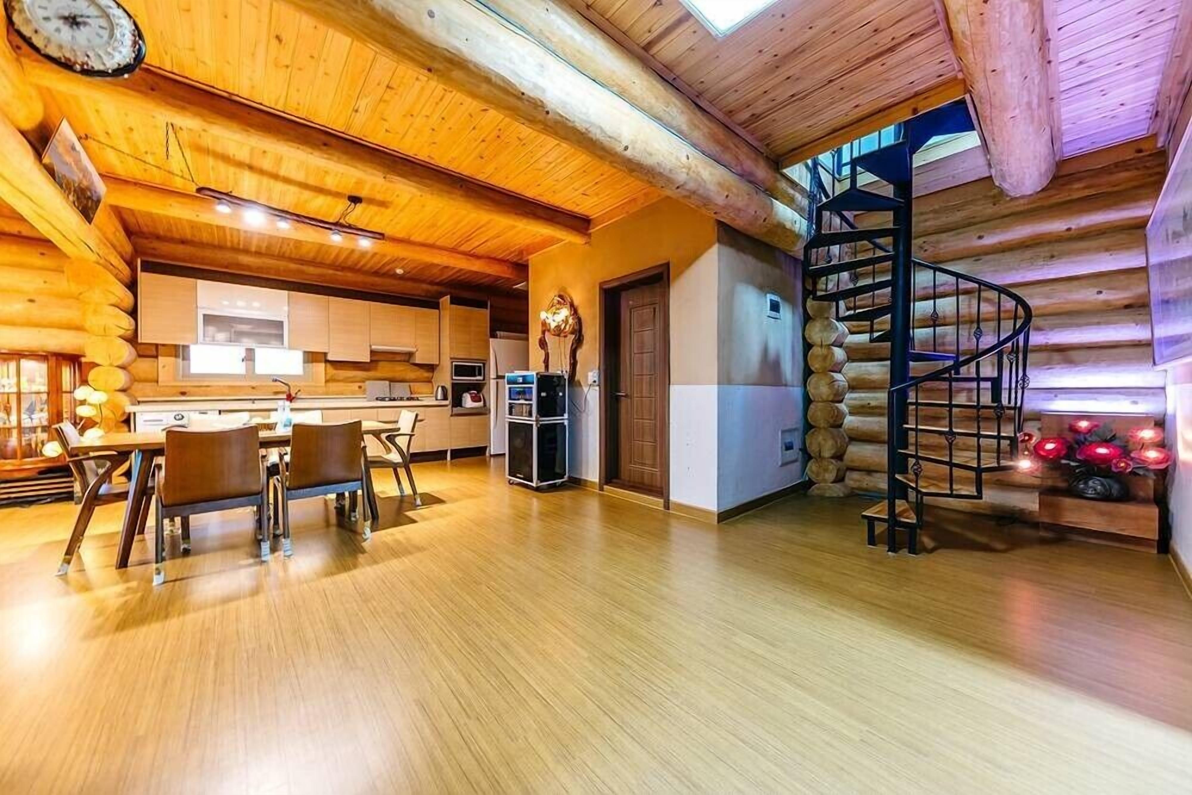 A log cabin interior with a dining area, kitchen, and a spiral staircase.