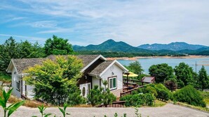 A two-story house with a balcony, surrounded by greenery and a lake view. - Hosu Ilchul Pension (Jecheon)